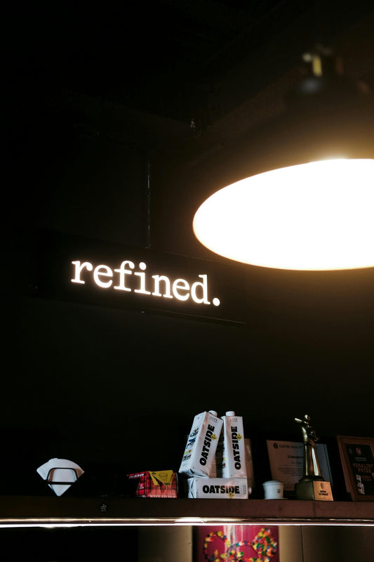 A neon sign that says refined above shelves.