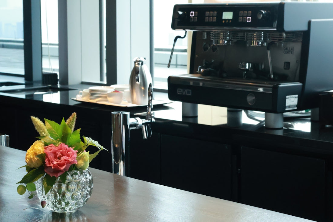 A modern coffee machine on a black counter with flowers.