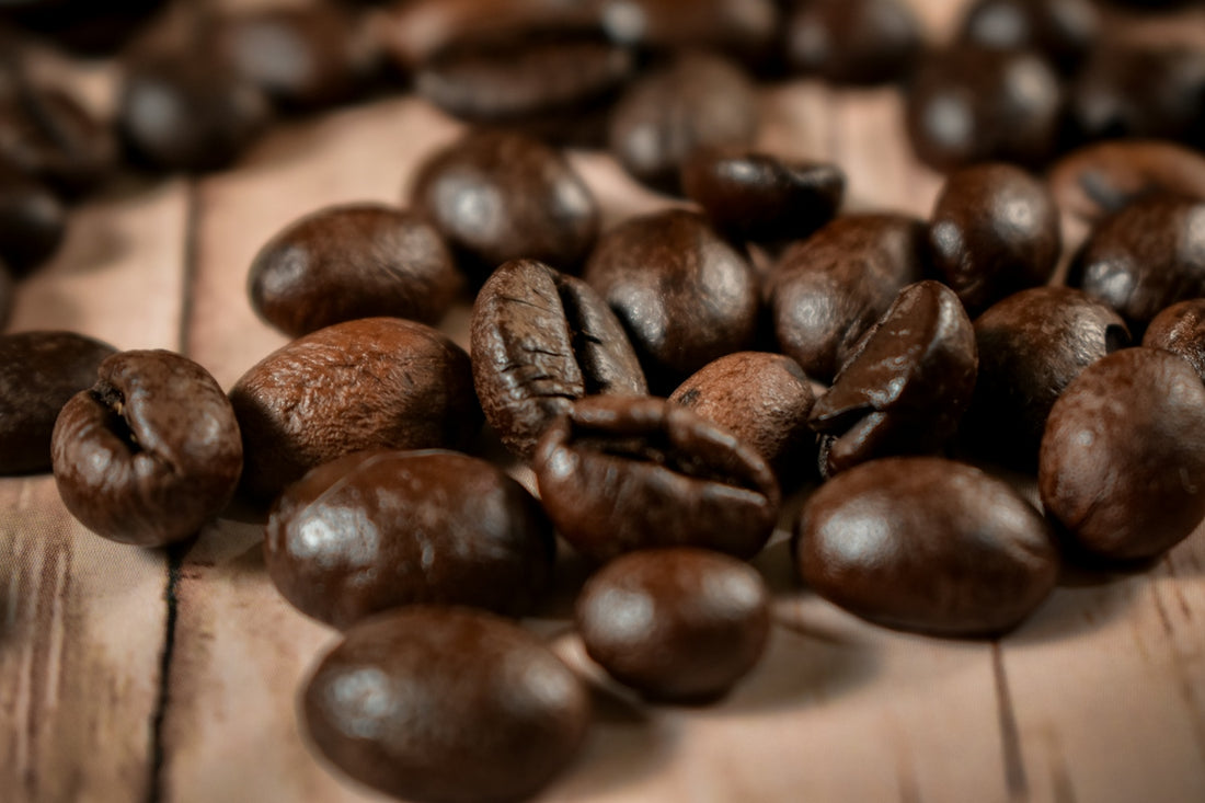 Dark roasted coffee beans scattered on a light wooden surface