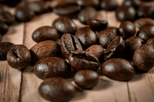 Dark roasted coffee beans scattered on a light wooden surface