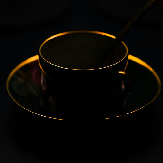 A dark teacup and saucer with a golden rim in low light